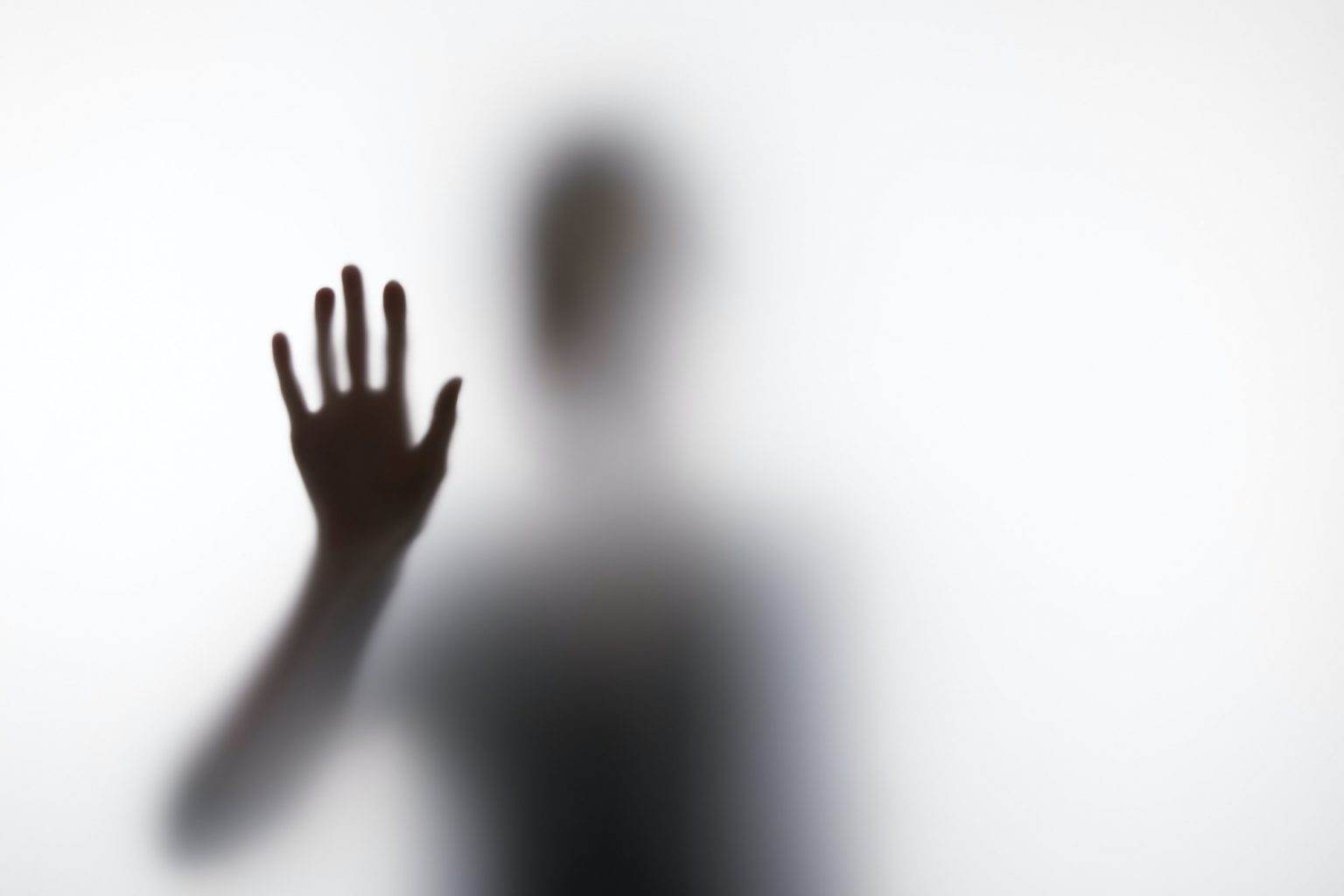 Blurry silhouette of person touching glass with hand
