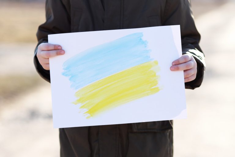 A small refugee boy from Ukraine with a drawing of the Ukrainian flag.