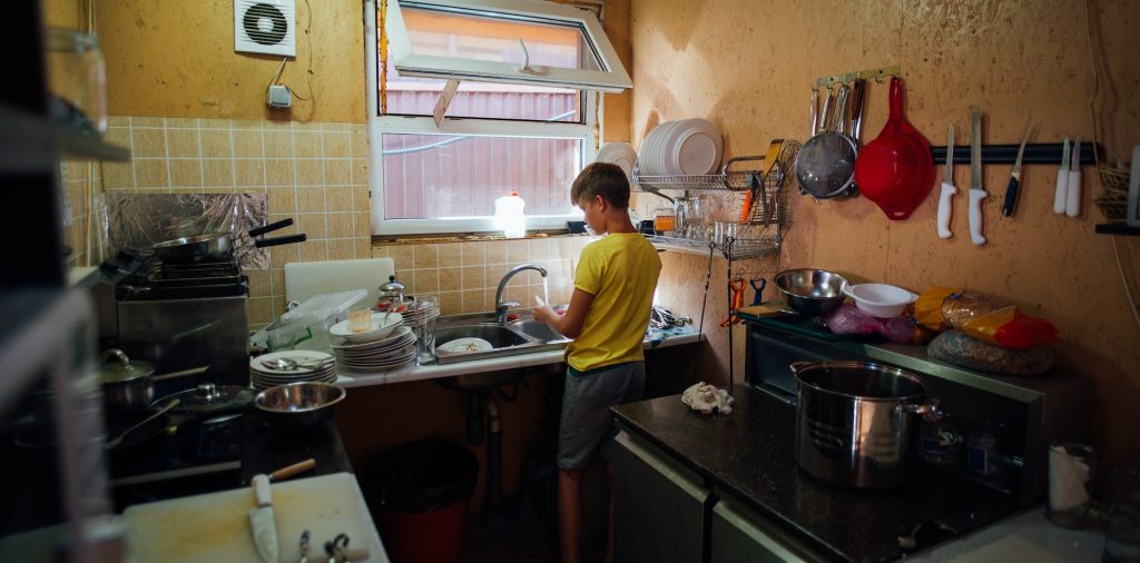 boy washing dishes in the kitchen in a yellow t-shirt